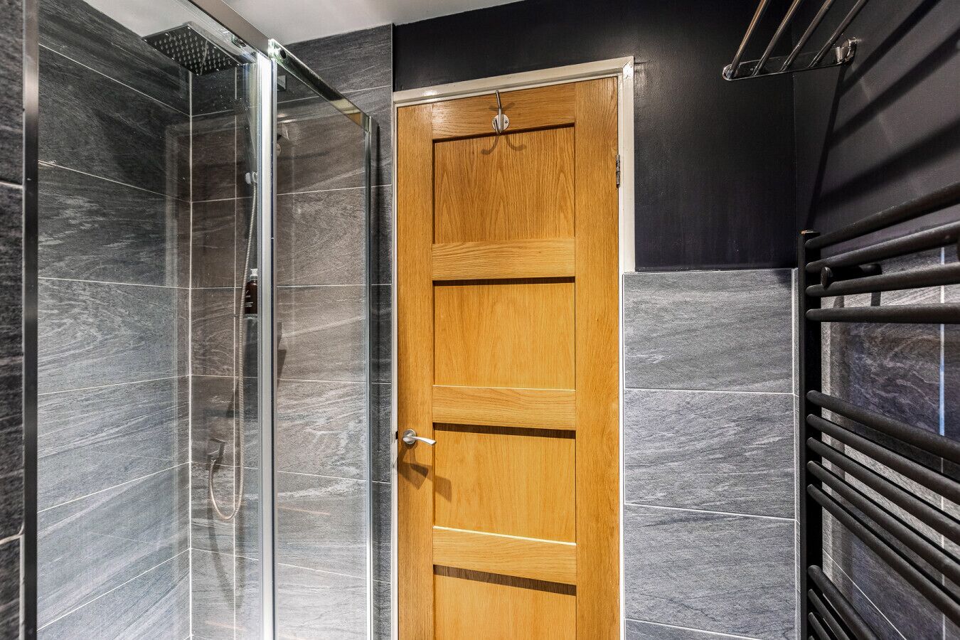 Un baño con cabina de ducha de vidrio, una puerta de madera y un perchero para toallas.