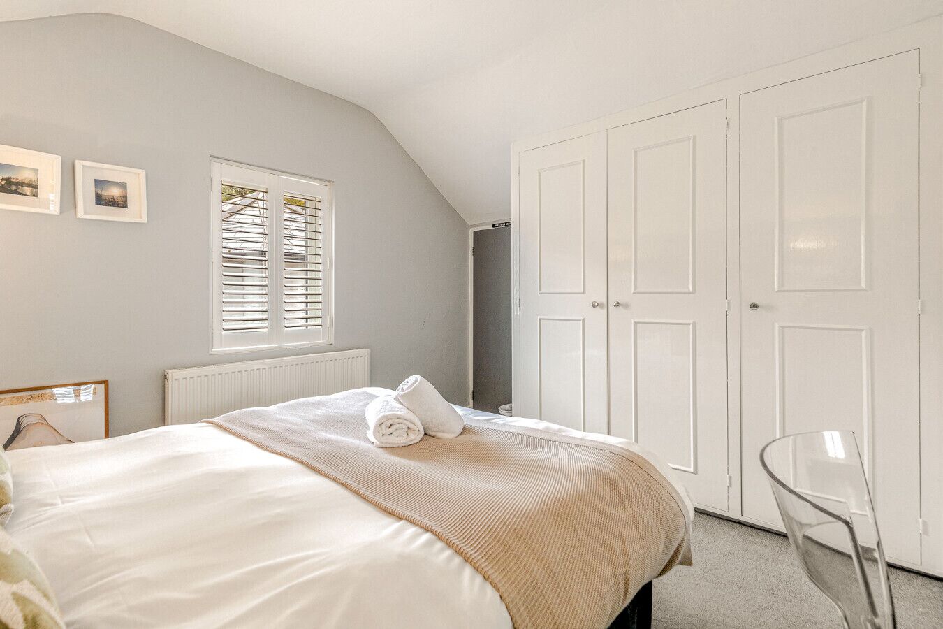 A bedroom with a bed, a radiator, a window with blinds, a wardrobe, and a chair.