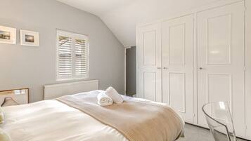 A bedroom with a bed, a radiator, a window with blinds, a wardrobe, and a chair.