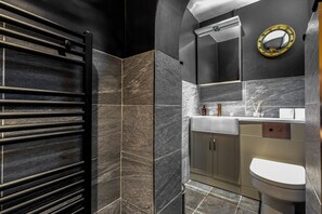 Un baño moderno con un toallero negro, un espejo con marco dorado y un inodoro.