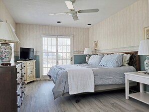A bedroom with a bed, a television, a dresser, a ceiling fan, and a window with blinds.