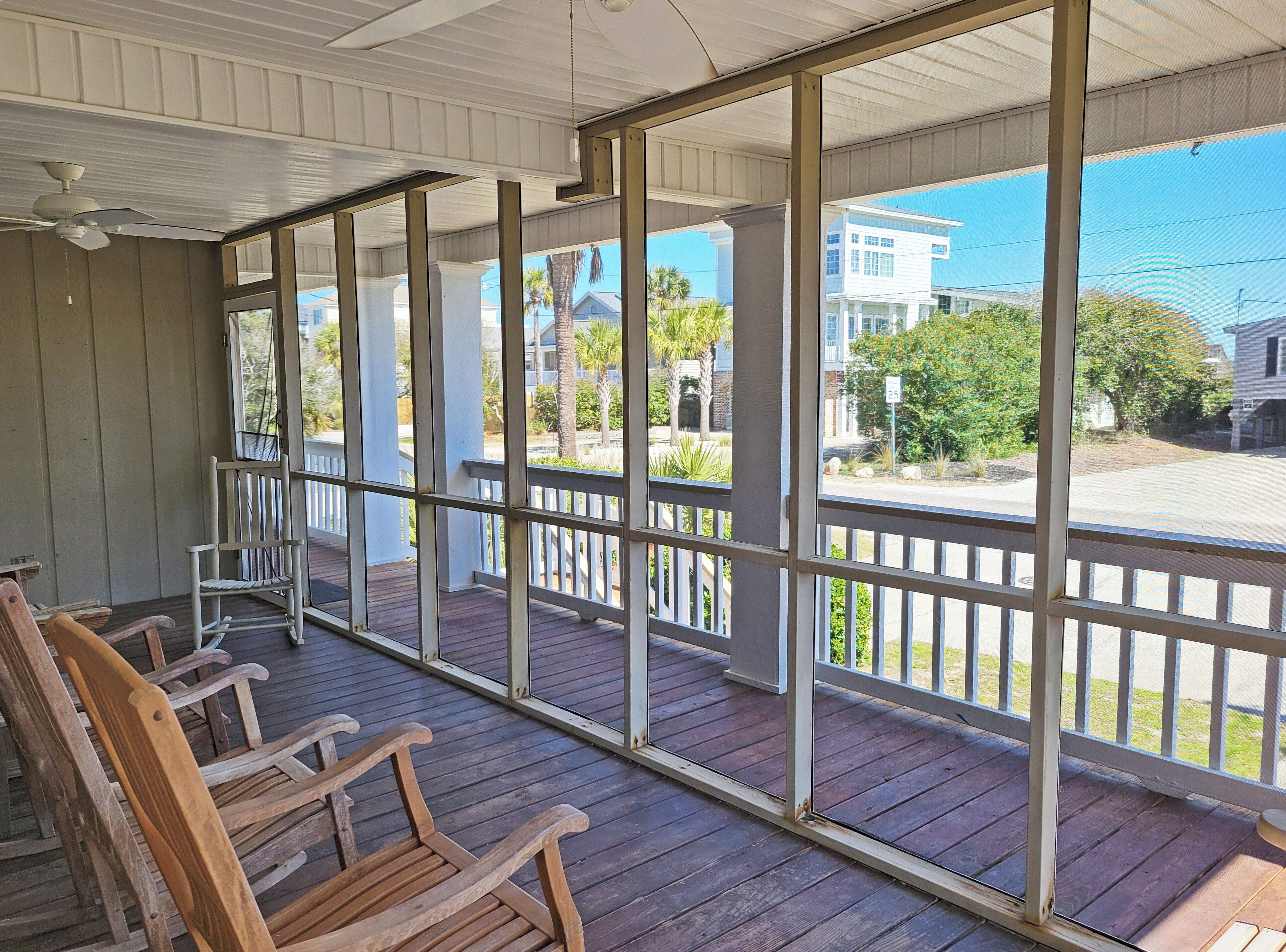 A covered porch with wooden chairs, a ceiling fan, and a view of a residential street.