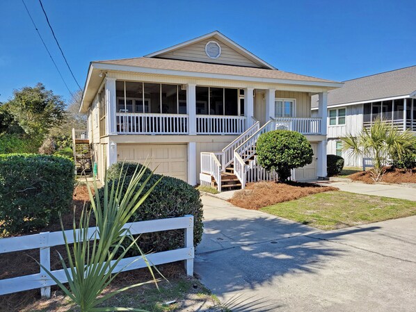 A two-story house with a covered porch, a front yard with a small tree, and a white picket fence.