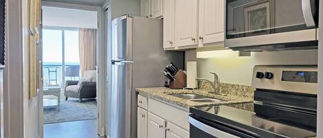 A modern kitchen with a refrigerator, microwave, oven, and granite countertop.