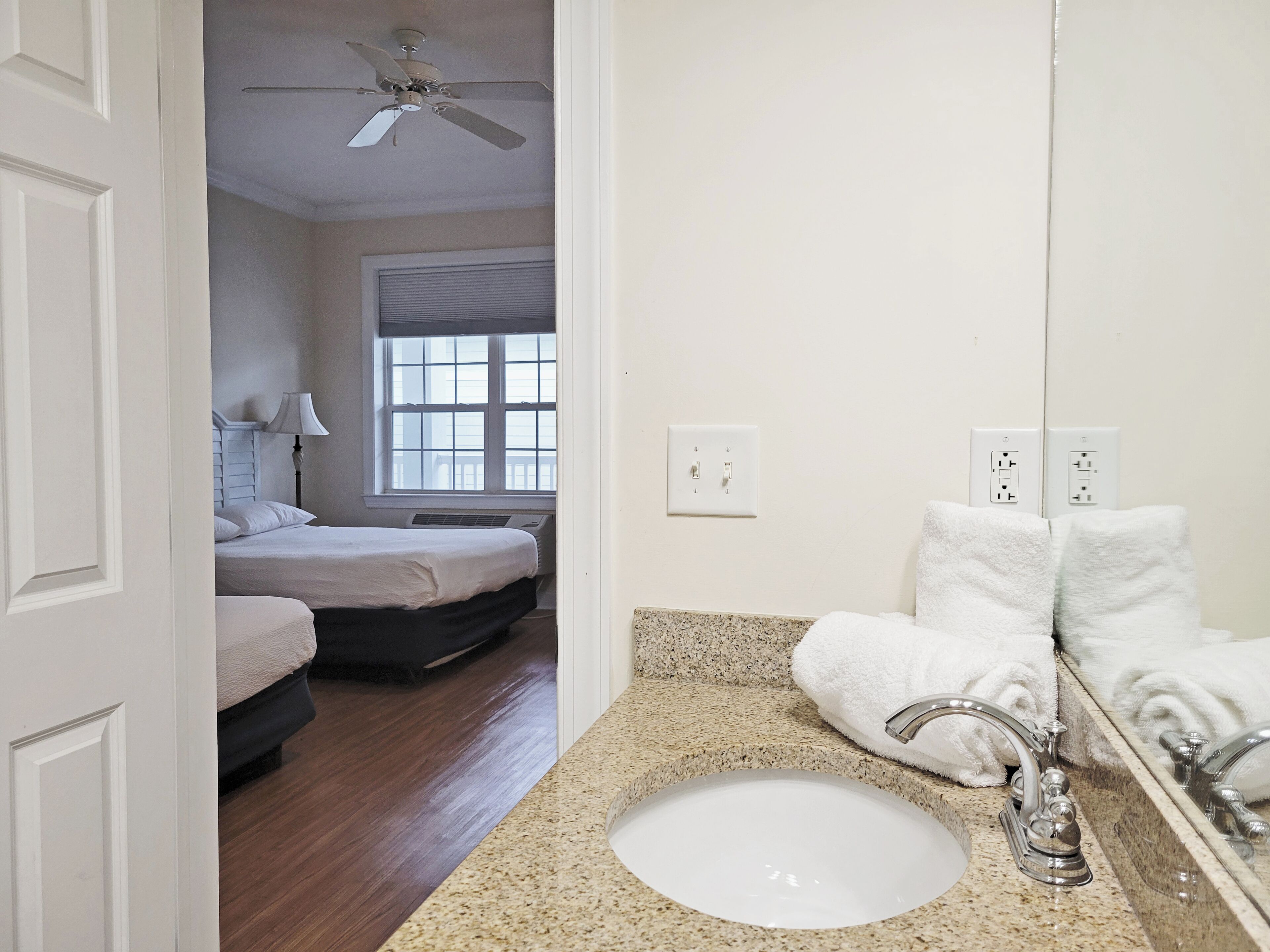 A hotel room with a bed, a bathroom with a sink and mirror, and a ceiling fan.