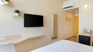 Una habitación de hotel moderna con televisión de pantalla plana, una mesita de noche, un escritorio pequeño con una silla, un espejo y una kitchenette con cafetera.