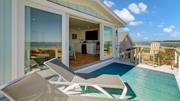 A modern villa with a glass-enclosed living area, a pool, and a view of the sea. - New Construction 5BR | Designer Coastal Home in Wild Dunes (Isle of Palms)