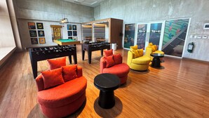 Un espace de détente moderne avec un plancher en bois, des canapés rouges et jaunes, une table de baby-foot et une table de billard.