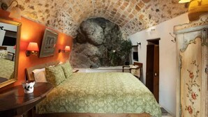 Une chambre avec un mur en pierre, un lit avec une literie verte, une commode en bois et un miroir.