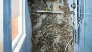 Une petite douche étroite avec un mur en marbre, une étagère contenant des articles de toilette et un plafond en bois.