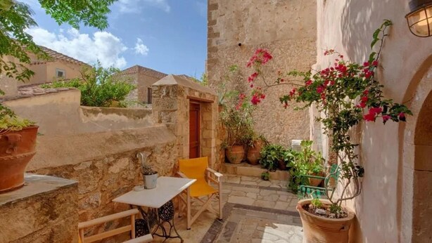 Une cour avec une table et des chaises, des plantes en pot et un mur en pierre.