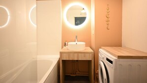 Een badkamer met een ronde spiegel, een wastafel, een badkuip en een wasmachine.