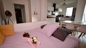 Een slaapkamer met een bed, een bureau en een kitchenette op de achtergrond.