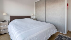 A neatly made bed with a white bedspread, a wooden headboard, and two bedside tables with lamps. - Flat for 2 adults and 1 child - View of the Port (La Baule-Escoublac)