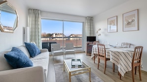 A modern living room with a sofa, chairs, a dining table, and a large window offering a city view. - Flat for 2 adults and 1 child - View of the Port (La Baule-Escoublac)