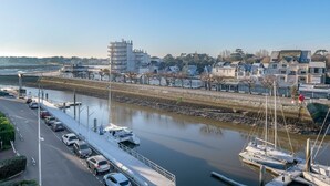 A marina with boats docked, a road parallel to the water, and buildings in the background. - Flat for 2 adults and 1 child - View of the Port (La Baule-Escoublac)