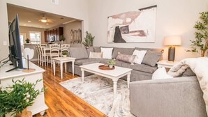 A living room with a grey sofa, white coffee table, and a dining area with wooden chairs and a table.