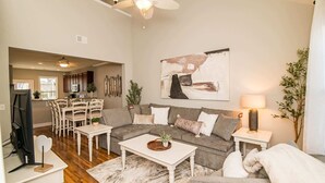 A spacious living room with a large gray sectional sofa, a white coffee table, and a dining area with wooden chairs and a small table.