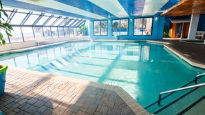 Una piscina interna con pareti in vetro trasparente, pavimento piastrellato e zona con panche.