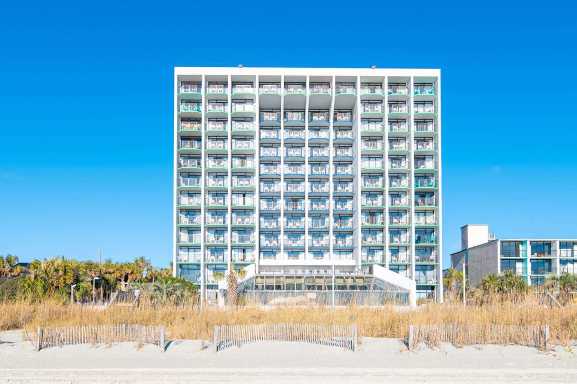 A high-rise hotel with multiple balconies, a central staircase, and a beach view.