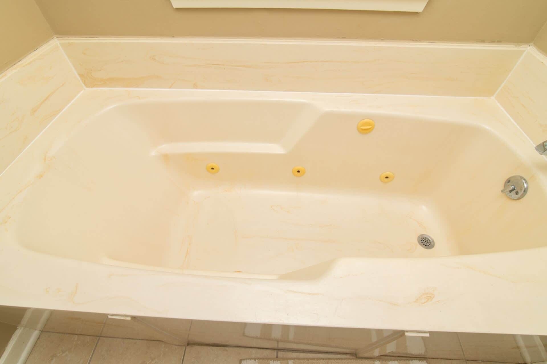 Une grande baignoire vide, avec un robinet et trois vannes jaunes.