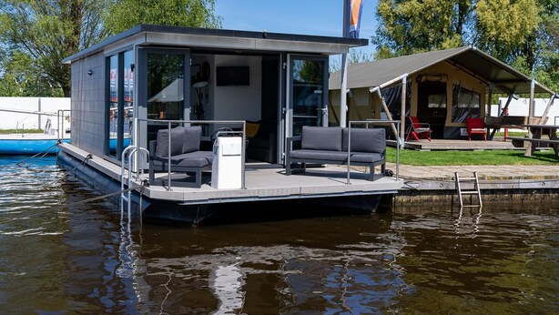 A floating houseboat with a covered deck, a small kitchen area, and a seating area with cushions. - Houseboat in Heeg With Stunning Marina Views (Heeg)