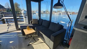 A covered outdoor seating area with a sofa, a small table, and a lamp. - Houseboat in Heeg With Stunning Marina Views (Heeg)