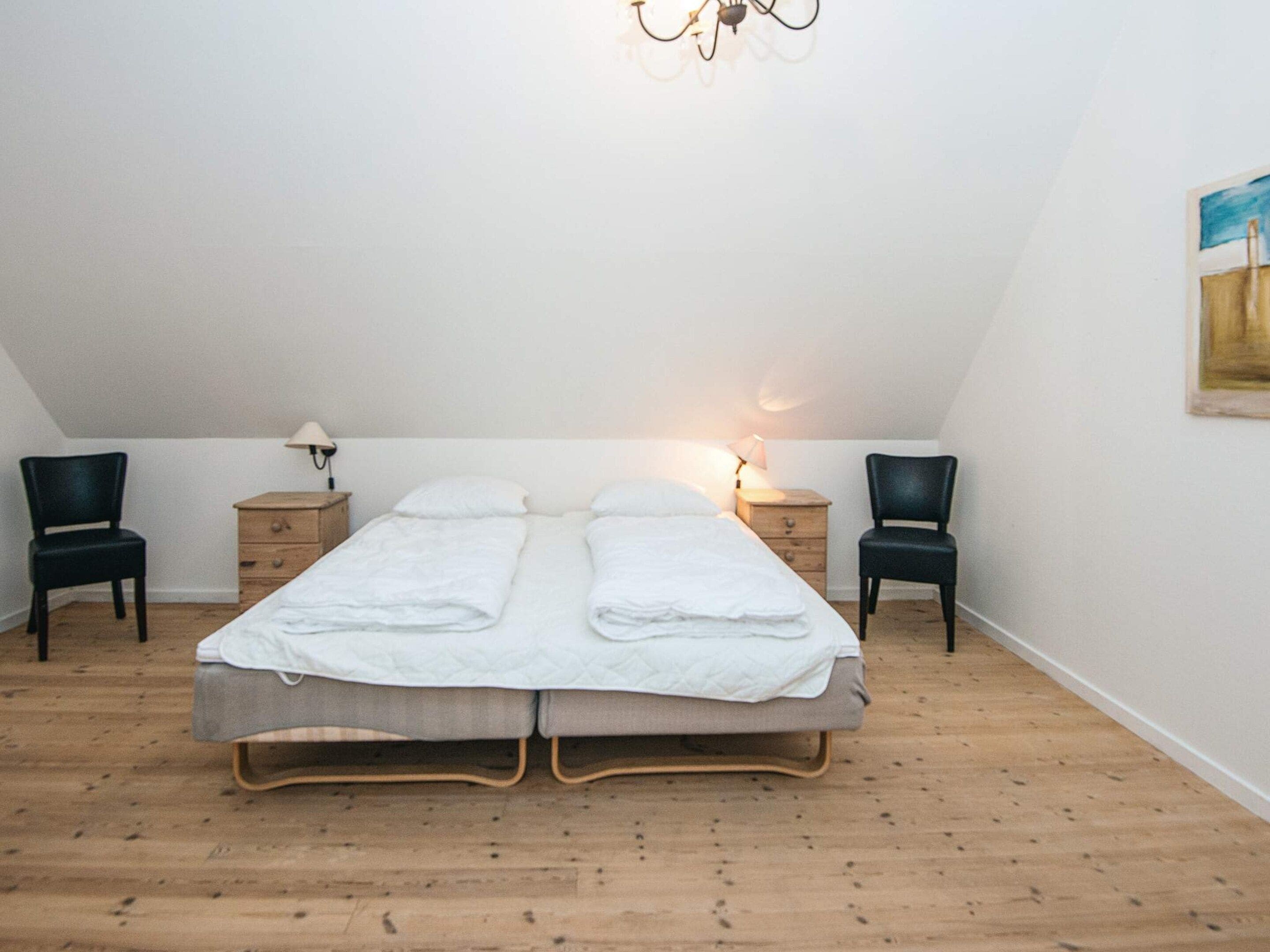 A bedroom with a bed, two chairs, two bedside tables, and a chandelier.