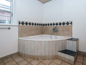 A corner bathroom with a bathtub, tiled walls, and a window.