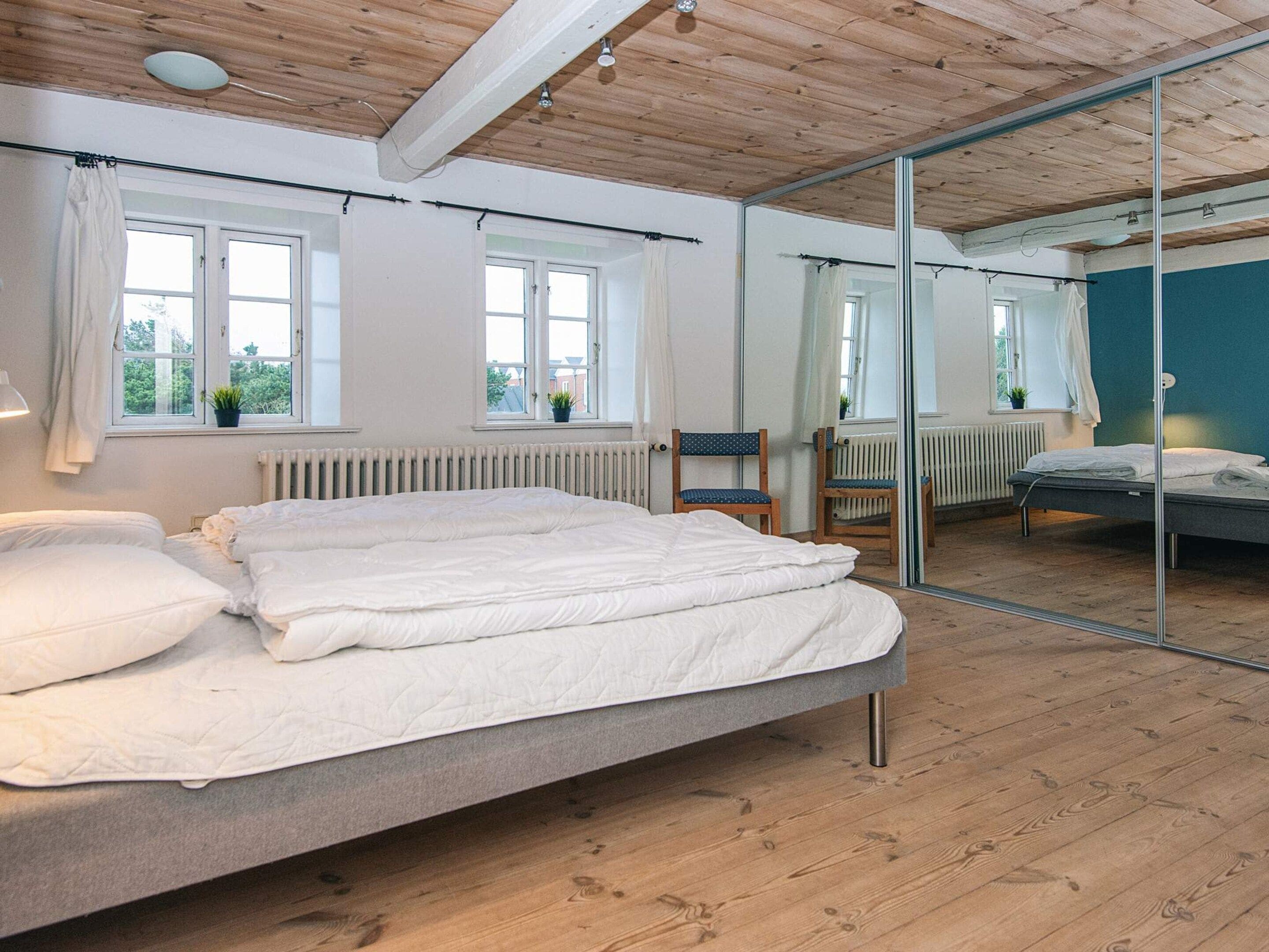 Ein Schlafzimmer mit einem Bett, einem Sessel, einem Fenster und einem Spiegel.