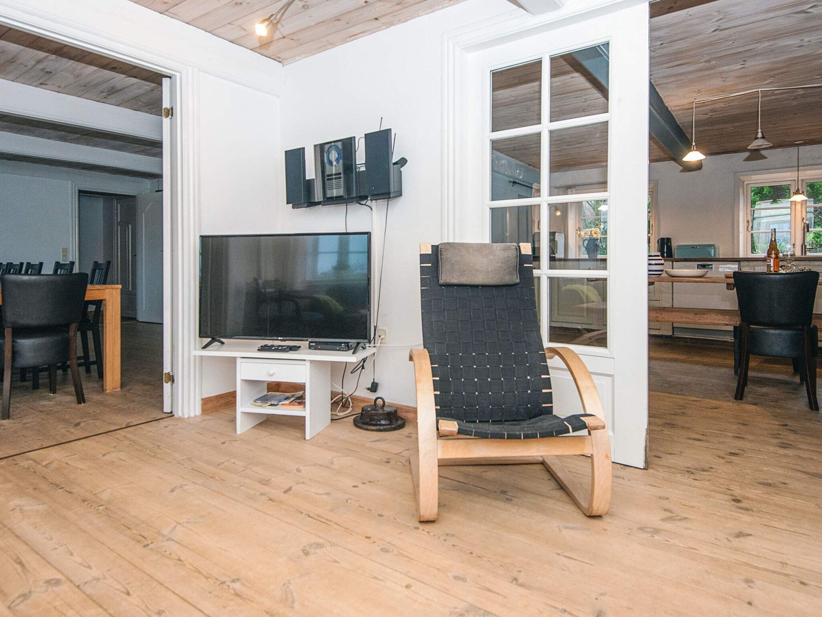 Ein modernes Wohnzimmer mit Fernseher, Holzboden und einer Sitzecke mit Sessel und Tisch.