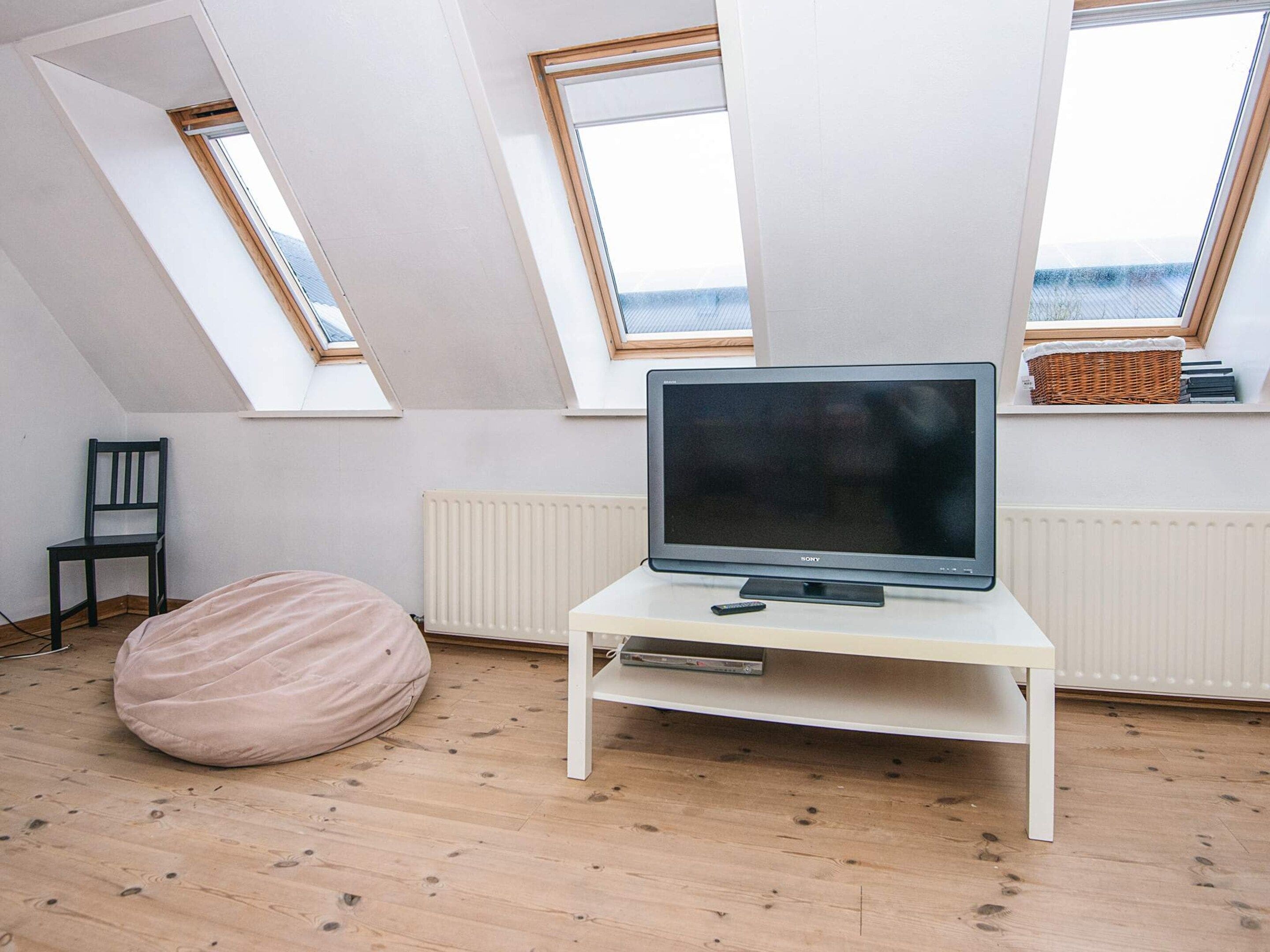 A room with a television on a white stand, a bean bag, a chair, and skylights.