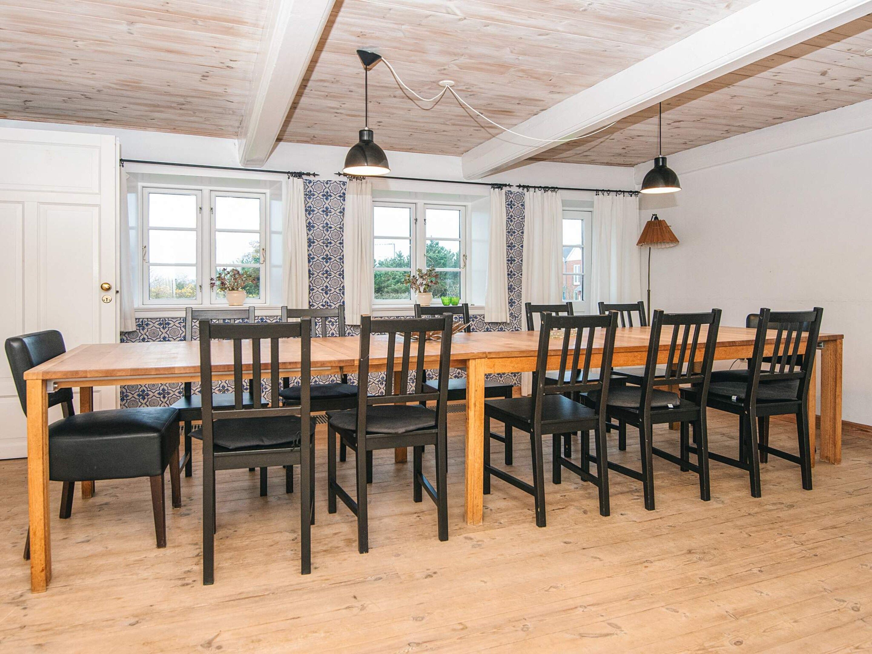Comedor con mesa y sillas de madera, ventanas amplias con cortinas e iluminación colgante.