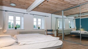 Quarto com cama, duas janelas, uma cadeira e um espelho grande.