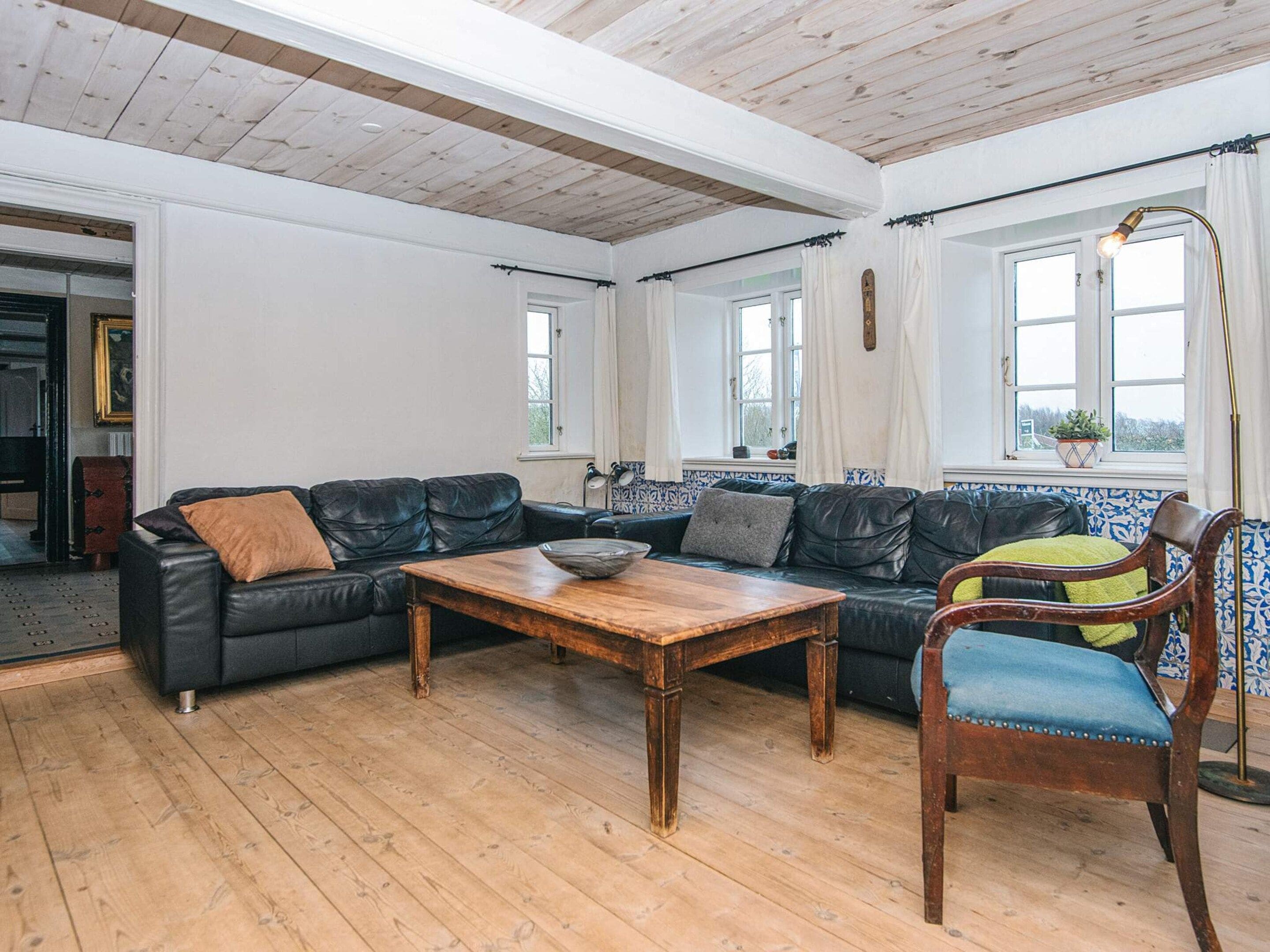 Una sala de estar con una mesa de centro de madera, sofás de cuero negro, un sillón tapizado en azul y vistas al exterior a través de ventanas.