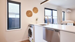 A compact kitchen with a washing machine, dishwasher, and a large window providing natural light. - Newly built unit in St Kilda. Modern amenities (Dunedin)