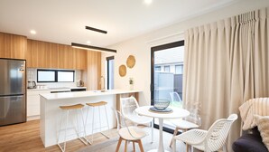 A modern kitchen with a central island, white bar stools, and a dining area with a round table and chairs. - Newly built unit in St Kilda. Modern amenities (Dunedin)