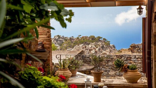 Une terrasse avec un mur en pierre, des plantes en pot et une table agrémentée d’une bougie et de tasses.