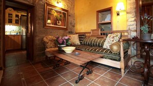 Un salon chaleureux avec un mur en pierre, des meubles en bois, un canapé, une table basse et, au fond, une cuisine.