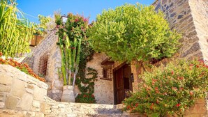 Un bâtiment en pierre avec une porte en bois, entouré de verdure et de fleurs.