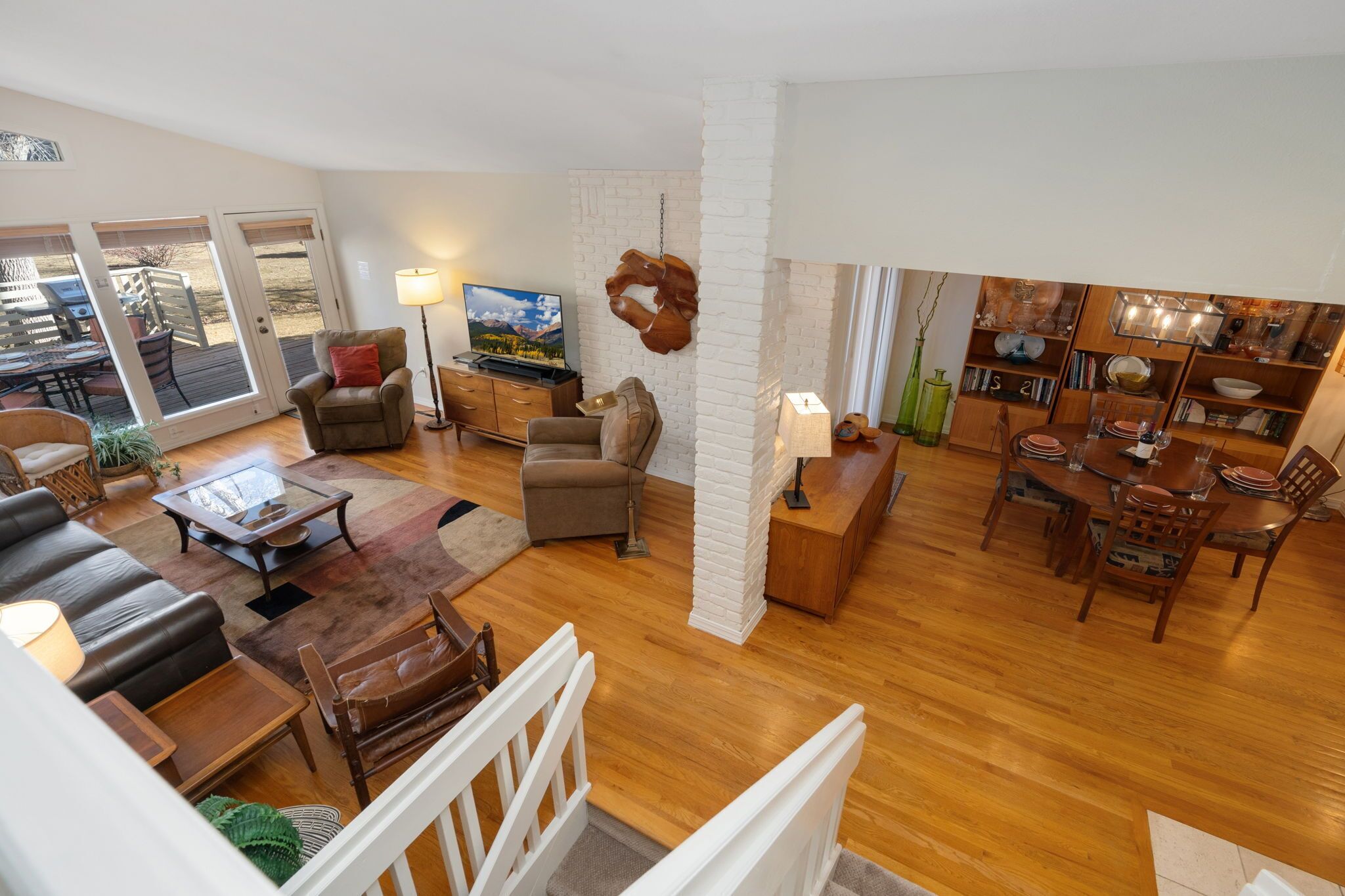 A spacious living area with a sofa, coffee table, and TV. There is a dining area with a table and chairs. The room has wooden flooring and white walls.