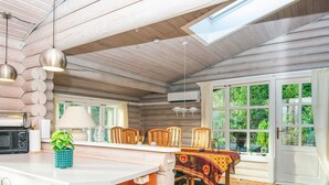 A cozy cabin interior with a wooden interior, a dining area with a table and chairs, and a large window offering a view of greenery outside. - 4 Star Holiday Home in Farvang (Farvang)