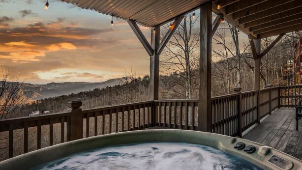 Ein Whirlpool mit Holzterrasse und Geländer mit Blick auf eine gebirgige Landschaft.