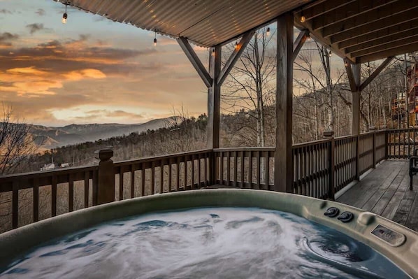 A hot tub with a wooden deck and railing, overlooking a mountainous landscape.