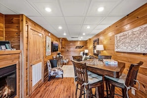 A wooden interior with a fireplace, dining table, chairs, and a map on the wall.