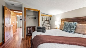 A bedroom with a wooden door, a bed with a white and brown bedspread, a hanging chair, and a coat rack. - Stunning Views at Chateau LeConte • Hot Tub (Gatlinburg)