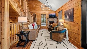 Ein rustikales Holzhaus-Interieur mit Treppe, Kamin, einer Couch und einem Esstisch.