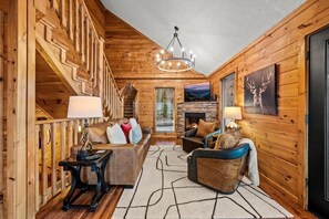 A log cabin interior with a staircase, a fireplace, a sofa, and a dining table.