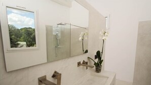 Une salle de bain dotée d’un grand miroir, d’un lavabo avec un robinet moderne et d’une fenêtre donnant sur un paysage verdoyant.