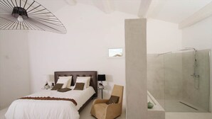 Une chambre à coucher comprenant un lit, une chaise, une table de chevet, une lampe et un espace douche.